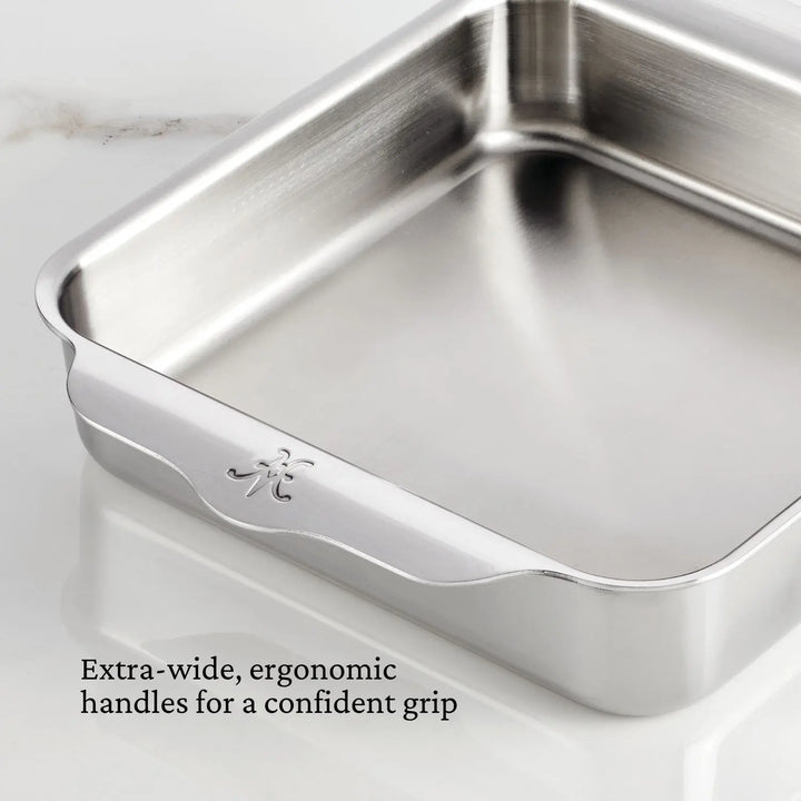 The Hestan OvenBond Tri-Ply 3-Piece Baking Set is displayed on a white marble surface. Extra-wide, ergonomic handles ensure a confident grip, as noted in black text at the bottom left.
