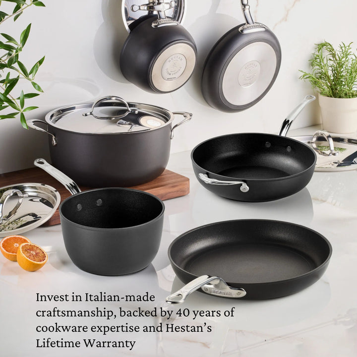 The TITUM® Fusion TITUM Nonstick Cookware Set, 10-Piece, features black and silver pots and pans with metal handles. Italian-made craftsmanship and a lifetime warranty are highlighted; some pieces hang on the wall while others sit on the kitchen surface.