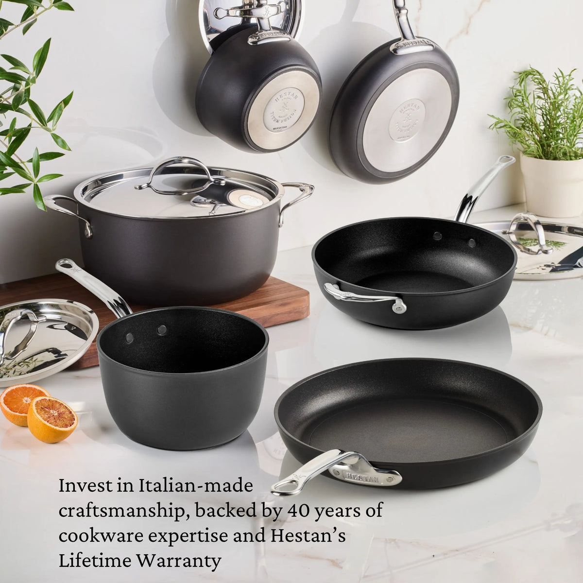 The TITUM® Fusion TITUM Nonstick Cookware Set, 10-Piece, features black and silver pots and pans with metal handles. Italian-made craftsmanship and a lifetime warranty are highlighted; some pieces hang on the wall while others sit on the kitchen surface.