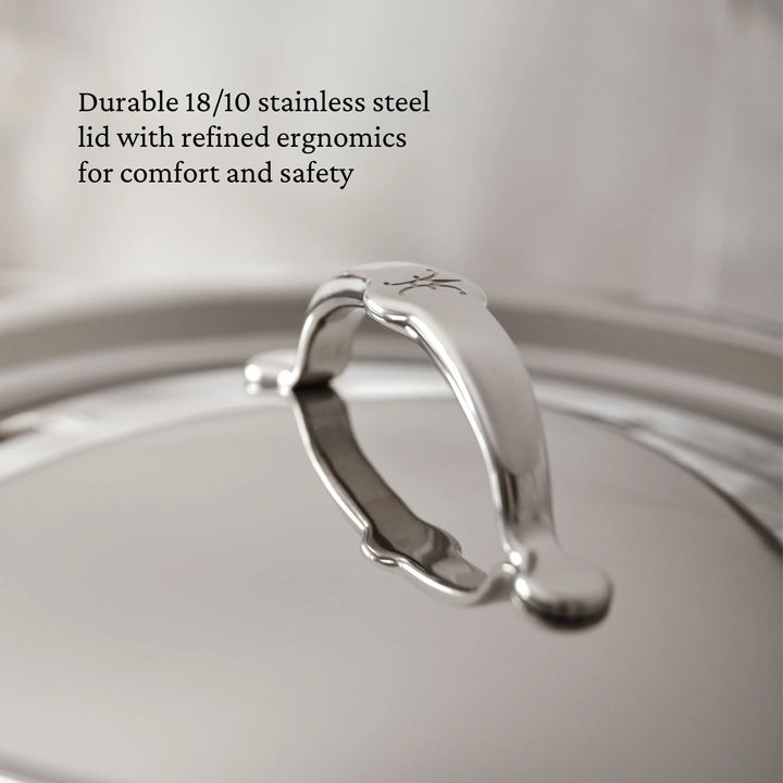 A close-up of the TITUM® Fusion TITUM Nonstick Essential Pan with Lid, 4.5-Quart, shows its curved handle, engraved logo, and sleek stainless steel finish—durable and ergonomic for induction cooking.