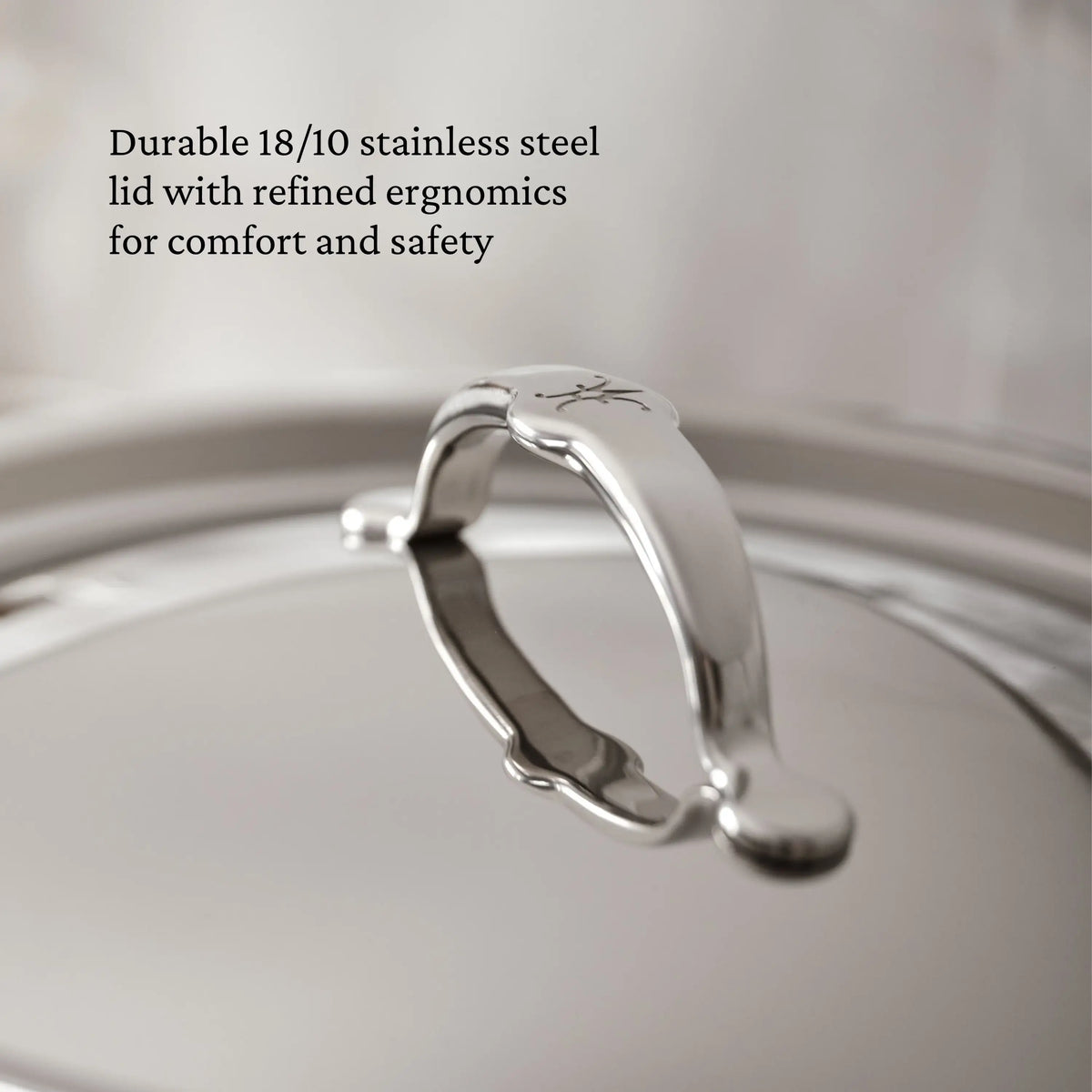 A close-up of the TITUM® Fusion TITUM Nonstick Essential Pan with Lid, 4.5-Quart, shows its curved handle, engraved logo, and sleek stainless steel finish—durable and ergonomic for induction cooking.
