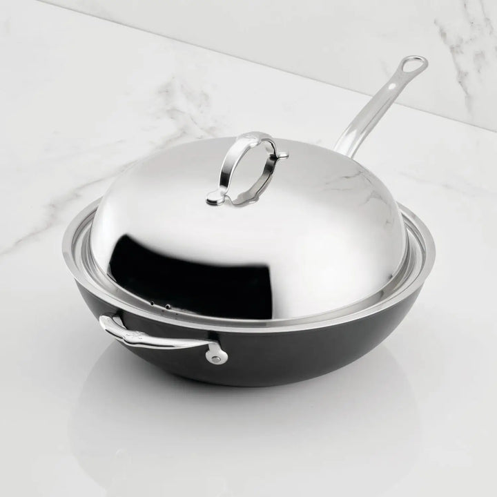 The TITUM® Fusion TITUM Nonstick Wok with Stick Handle and Dome Lid, 12.5-Inch, featuring a side handle, combines functionality and elegance on a white marble surface.