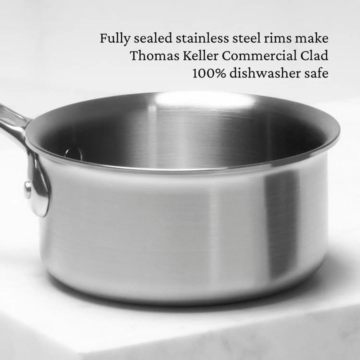 A Thomas Keller Commercial Clad 0.75-quart stainless steel butter warmer with handle sits on a white countertop. Text above reads: Fully sealed rims make it 100% dishwasher safe chef-designed tri-ply cookware.