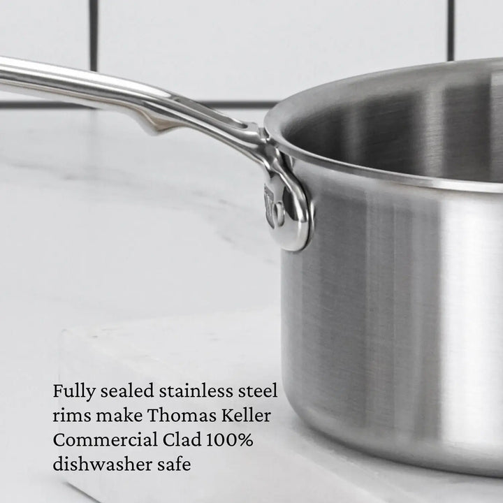 A close-up of the Thomas Keller Commercial Clad Stainless Steel Saucepan with handle on a white surface. Text highlights its fully sealed rims and 100% dishwasher safe design—ideal for professional results.