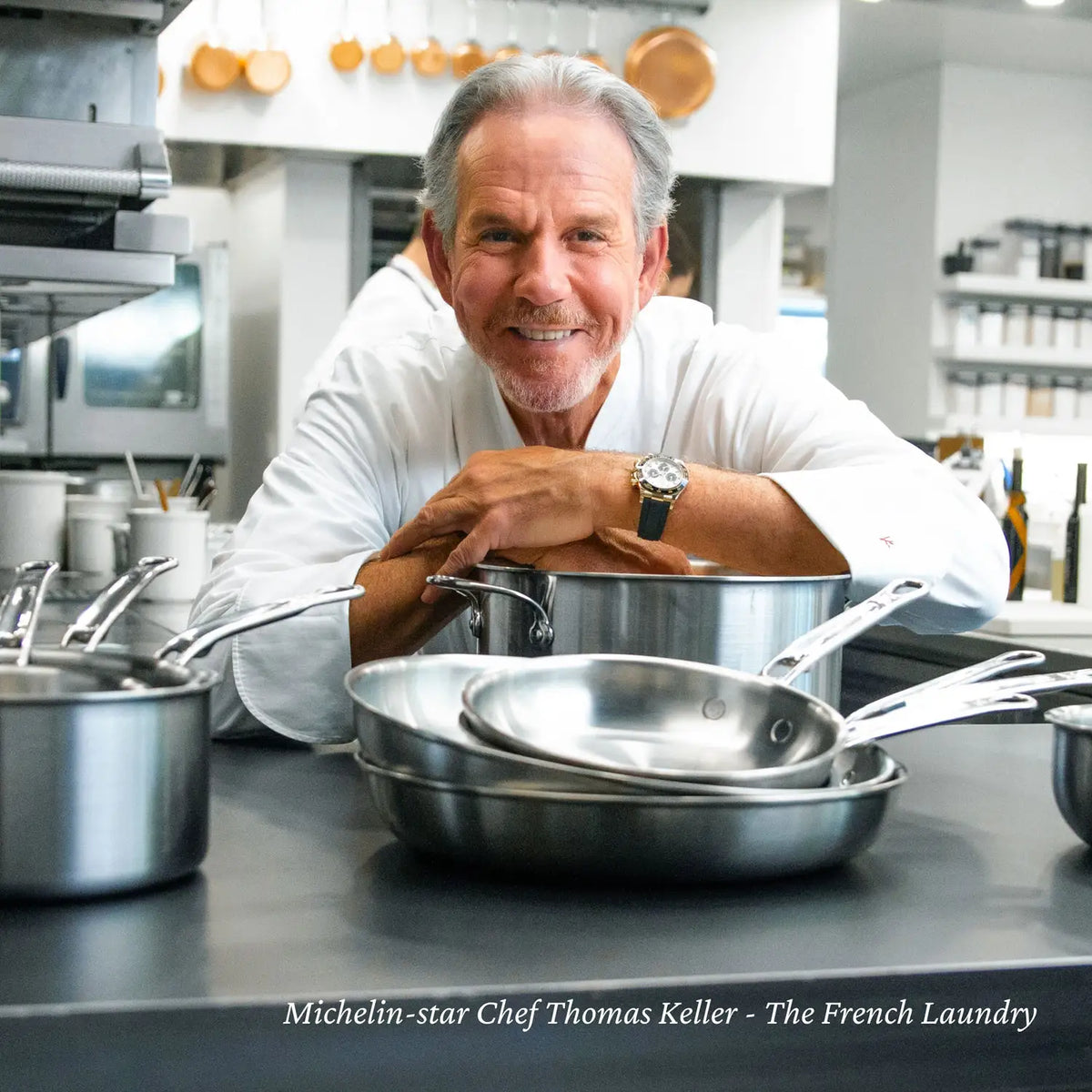 A chef in a white coat leans on a kitchen counter with Thomas Keller Commercial Clad Stainless Steel Rondeaus in a professional kitchen. Text at the bottom reads: Michelin-star Chef Thomas Keller - The French Laundry.