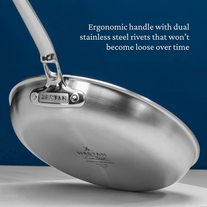 A Thomas Keller Commercial Clad Stainless Steel Skillet shown from below highlights its ergonomic handle with dual stainless steel rivets. The skillet’s handle and rivets are designed for lasting durability—never loosening over time.