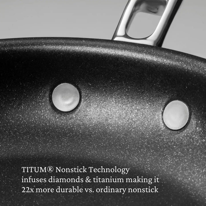 Close-up of a Thomas Keller Commercial Clad Stainless Steel TITUM® Nonstick Skillet, showing visible rivets and handle. Features TITUM® Nonstick Technology with diamonds and titanium for 22x greater professional performance.