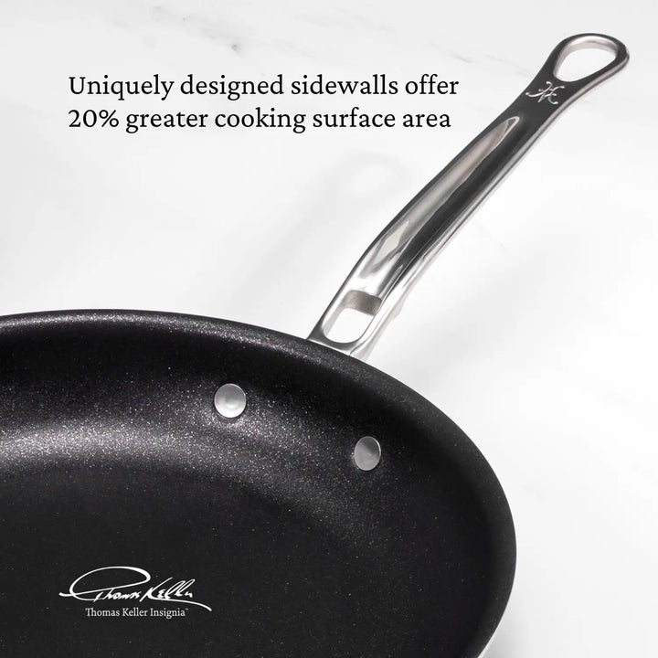 Close-up of a Thomas Keller Commercial Clad Stainless Steel TITUM® Nonstick Skillet with a shiny metal handle on a white surface. Above, it reads, “Uniquely designed sidewalls offer 20% greater cooking surface area.” Signature in lower-left corner.