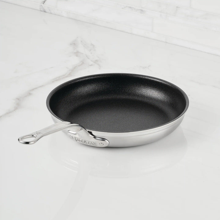 A ProBond® Forged™ Brushed Clad Stainless Steel TITUM® Nonstick Skillet with a black nonstick interior sits on a white marble countertop. The handle is engraved with "ProBond®".