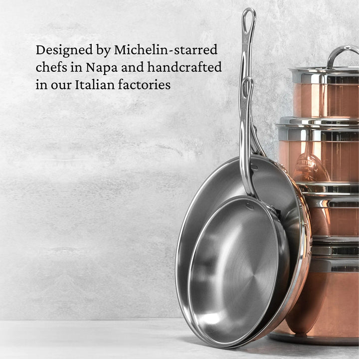 Two metal frying pans rest against a stack of CopperBond's Copper Induction Set, 24-Piece, on a kitchen counter. Wall text highlights its design by Michelin-starred chefs in Napa and expert handcrafting in Italy.