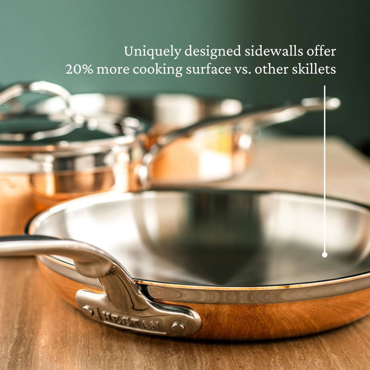 A close-up shows the CopperBond Copper Induction Set, 24-Piece—handcrafted in Italy—on a wooden surface with other cookware, highlighting its 20% larger cooking surface compared to standard skillets.