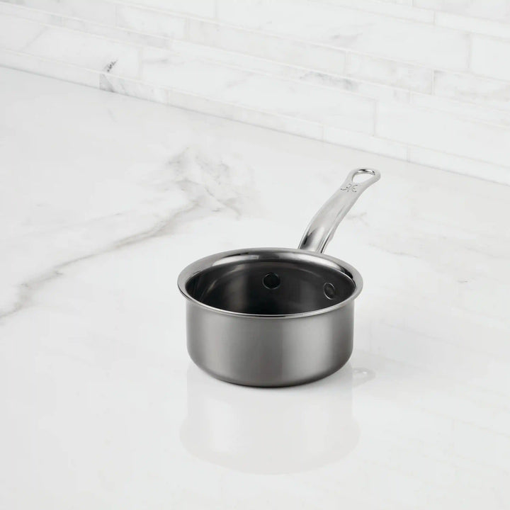A NanoBond Titanium Butter Warmer (.75 quarts) with a long handle sits on a white marble countertop against a tiled backsplash, making it an elegant and stylish choice for warming butter.
