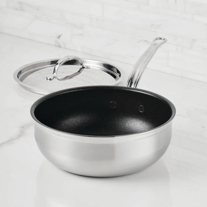 A ProBond® Forged™ Professional Clad Stainless Steel TITUM® Nonstick Essential Pan, 3.5-Quart, is shown on a white countertop with a long handle and its matching stainless steel cover placed beside it.