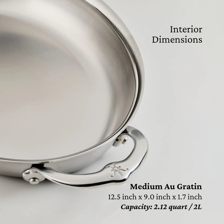 A close-up of the Hestan Provisions 15-Inch x 9-Inch Oval Au Gratin baker highlights its handle and interior, showing text with its size and ample capacity for versatile baking.