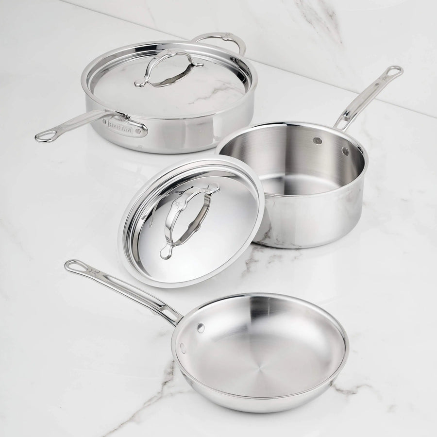The ProBond® Luxe™ Polished Clad Stainless Steel Signature Set, 5-Piece, features tri-ply cookware: a sauté pan with lid, saucepan with lid, and frying pan, all induction-suitable with metal handles and polished finishes on a white marble surface.
