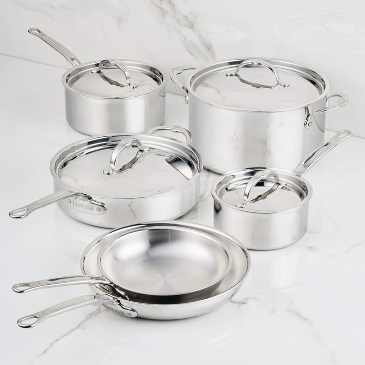 The ProBond® Luxe™ Polished Clad Stainless Steel Ultimate Set, 10-Piece, features saucepans, a frying pan, and a stock pot with lids—each boasting polished surfaces and metal handles, arranged on a white marble countertop.