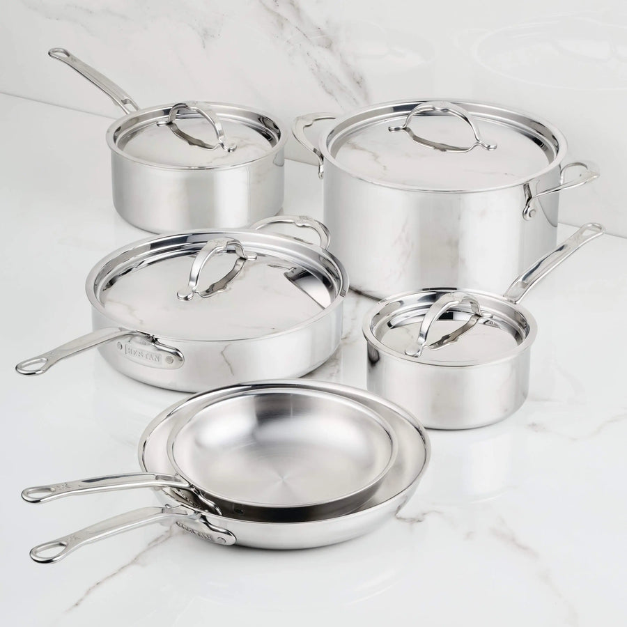 The ProBond® Luxe™ Polished Clad Stainless Steel Ultimate Set, 10-Piece, features saucepans, a frying pan, and a stock pot with lids—each boasting polished surfaces and metal handles, arranged on a white marble countertop.