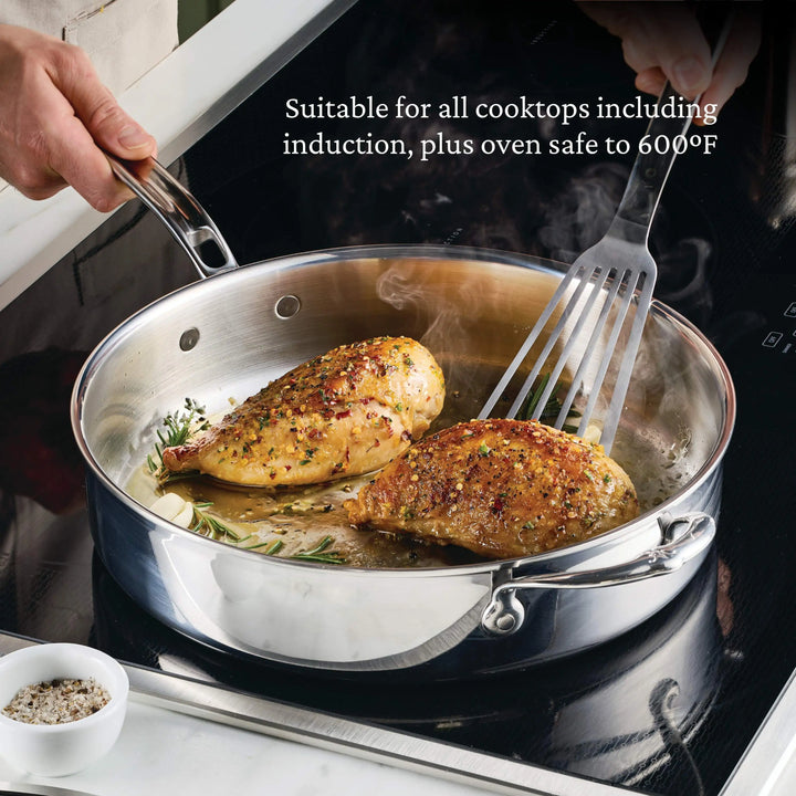 A person cooks two seasoned chicken breasts in a stainless steel pan using a spatula; text above highlights the Italian craftsmanship of the ProBond® Luxe™ Polished Clad Stainless Steel Ultimate Set, 10-Piece, safe to 600°F and induction compatible.
