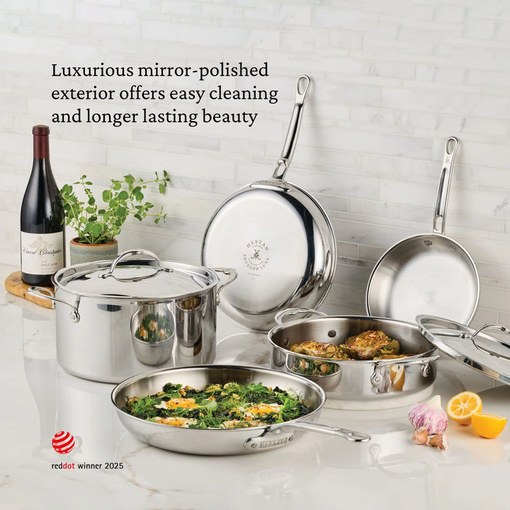ProBond® Luxe™ Professional Clad Stainless Steel Essential Pans with Lid are displayed on a kitchen counter filled with cooked food, surrounded by a wine bottle, herbs, lemon, and a wooden board—highlighting Italian craftsmanship and easy-clean durability.