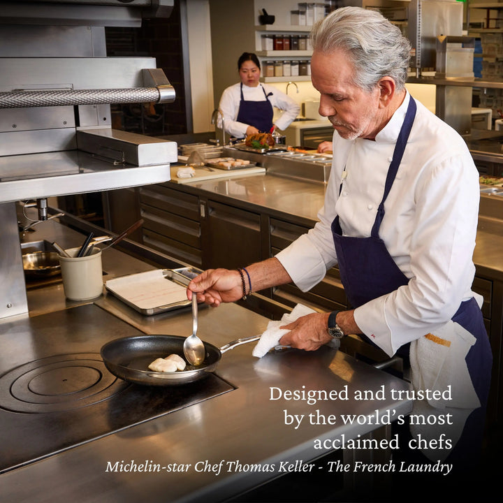 A chef sears scallops in ProBond® Luxe™ Polished Clad Stainless Steel Skillets with TITUM® Nonstick at a commercial kitchen, while another chef prepares food. Text credits Michelin-star Chef Thomas Keller of The French Laundry and Hestan.