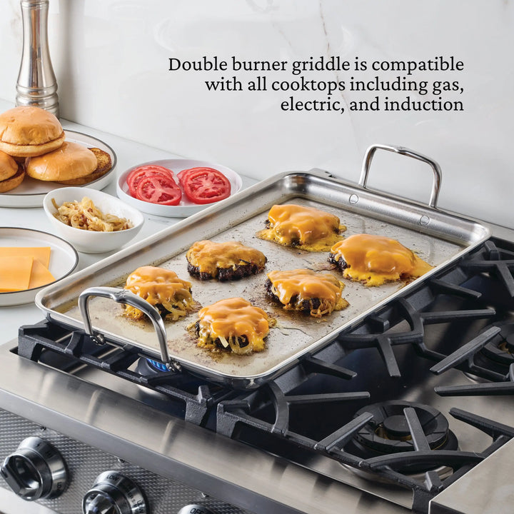 A NanoBond Titanium x Tyler Florence 41-piece cookware set double burner griddle cooks six cheeseburgers on a gas stove, while plates with buns, tomato slices, grilled onions, and cheese wait nearby. Cooktop compatibility details are displayed.