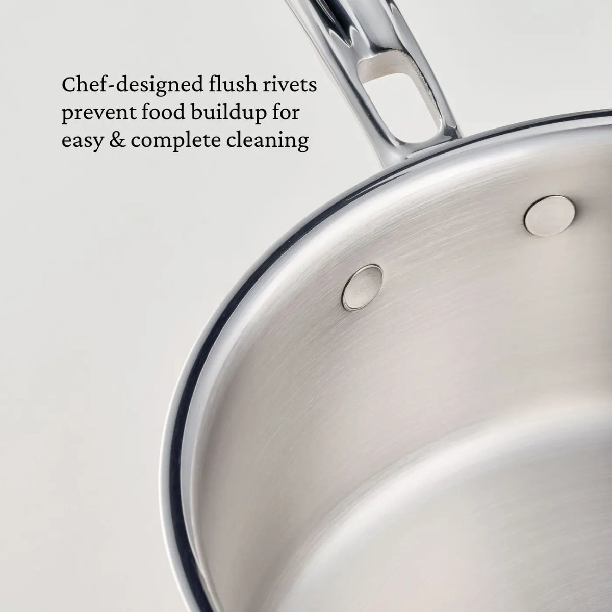 Close-up of a stainless steel saucepan from the CopperBond® Aura™ Polished Copper 10-Piece Cookware Set, featuring smooth, flush rivets that securely attach the handle. Text on the image reads: Chef-designed flush rivets prevent food buildup for easy & thorough cleaning.