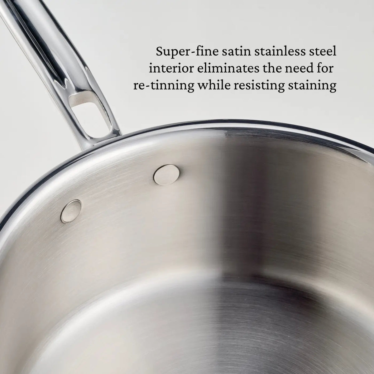 Close-up of a stainless steel saucepan from the CopperBond® Aura™ Polished Copper 10-Piece Cookware Set, featuring a super-fine satin stainless steel interior that resists staining and eliminates the need for re-tinning—a stunning addition to any copper cookware collection.