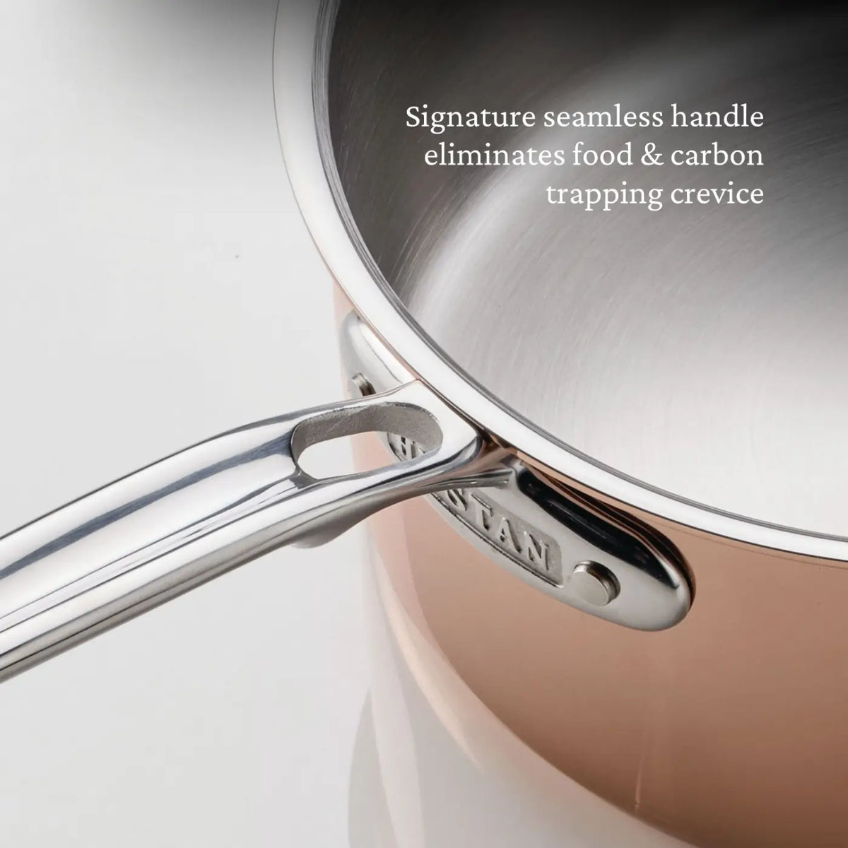 A close-up of a CopperBond Aura™ Polished Copper Saucepan with Lid highlights its seamless stainless steel handle, shown from above. Text on the image reads, Signature seamless handle eliminates food & carbon trapping crevice.