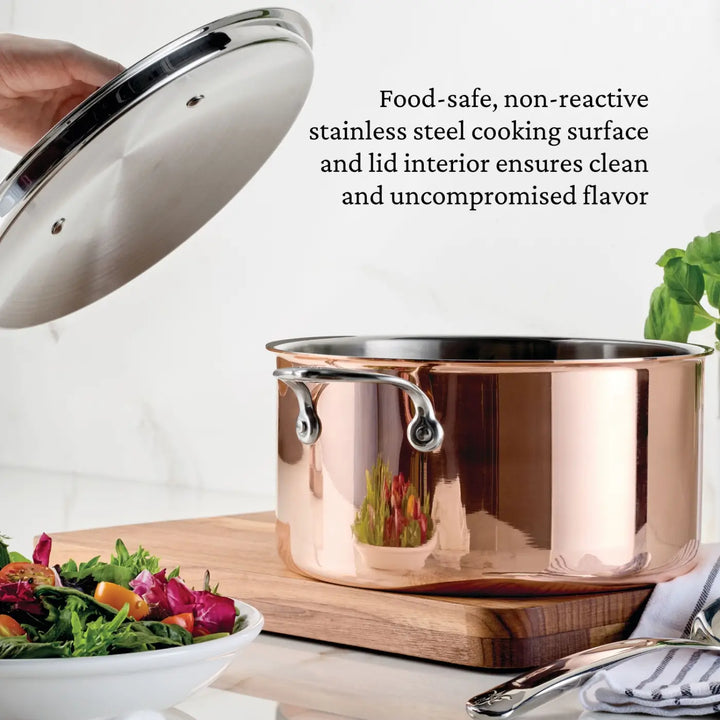 A hand lifts the lid off a CopperBond Aura™ Polished Copper Stock Pot with Lid, showcasing its stainless steel interior, on a counter beside a fresh salad, herbs, and utensils. Text alongside highlights that both the lid and pot are food-safe and non-reactive, preserving clean, uncompromised flavor.