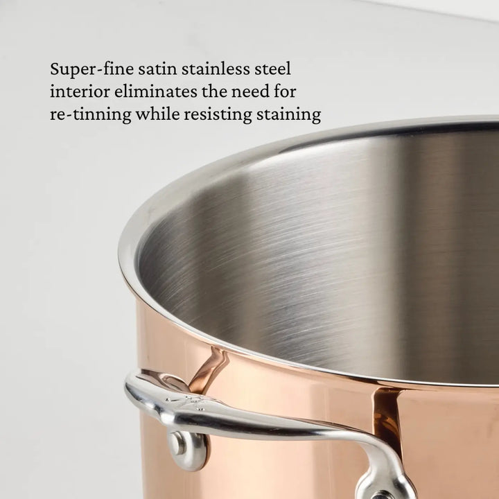 A close-up of the CopperBond Aura™ Polished Copper Stock Pot with Lid highlights its premium craftsmanship, featuring a satin stainless steel interior. The pot’s metal handle is securely fastened, while a brief description of the satin stainless steel interior appears in black text in the upper left corner.