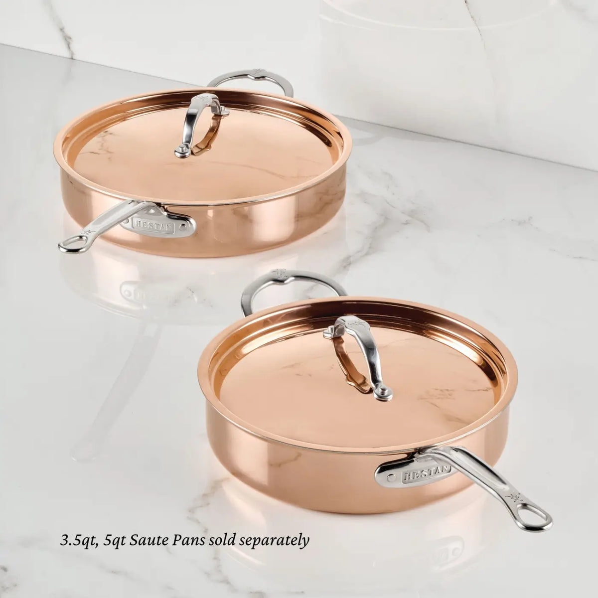 Two CopperBond Aura™ Polished Copper Sauté Pans with lids and stainless steel handles rest on a white marble surface, highlighting the sophistication of luxury copper cookware. The text reads: 3.5qt and 5qt Polished Copper Sauté Pans sold separately—each crafted with a durable stainless steel interior for outstanding cooking performance.