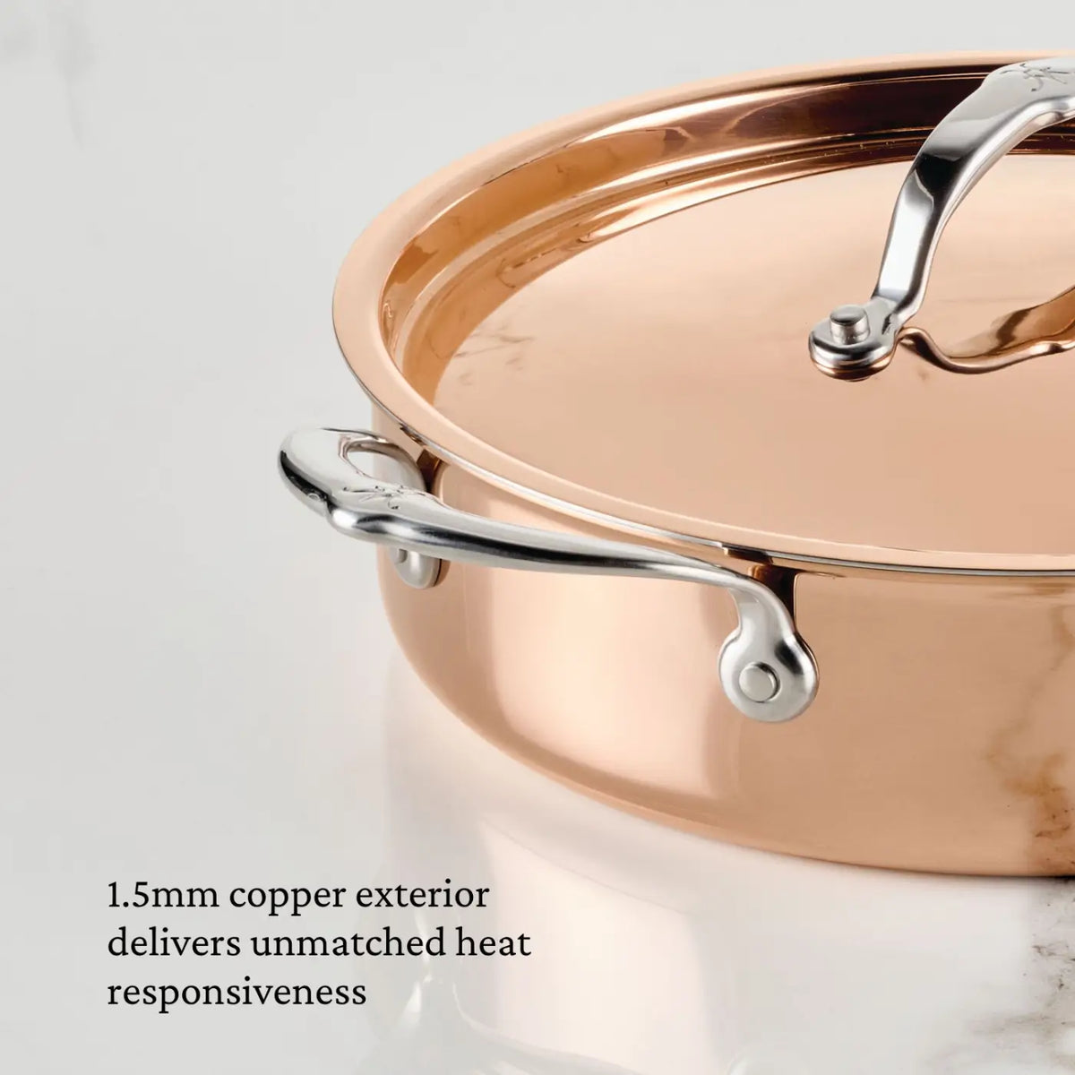 A close-up of the CopperBond Aura™ Polished Copper Rondeaus with Lid, Italian crafted and featuring stainless steel handles, sits on a white marble surface. Text reads: 1.5mm copper exterior delivers unmatched heat responsiveness.
