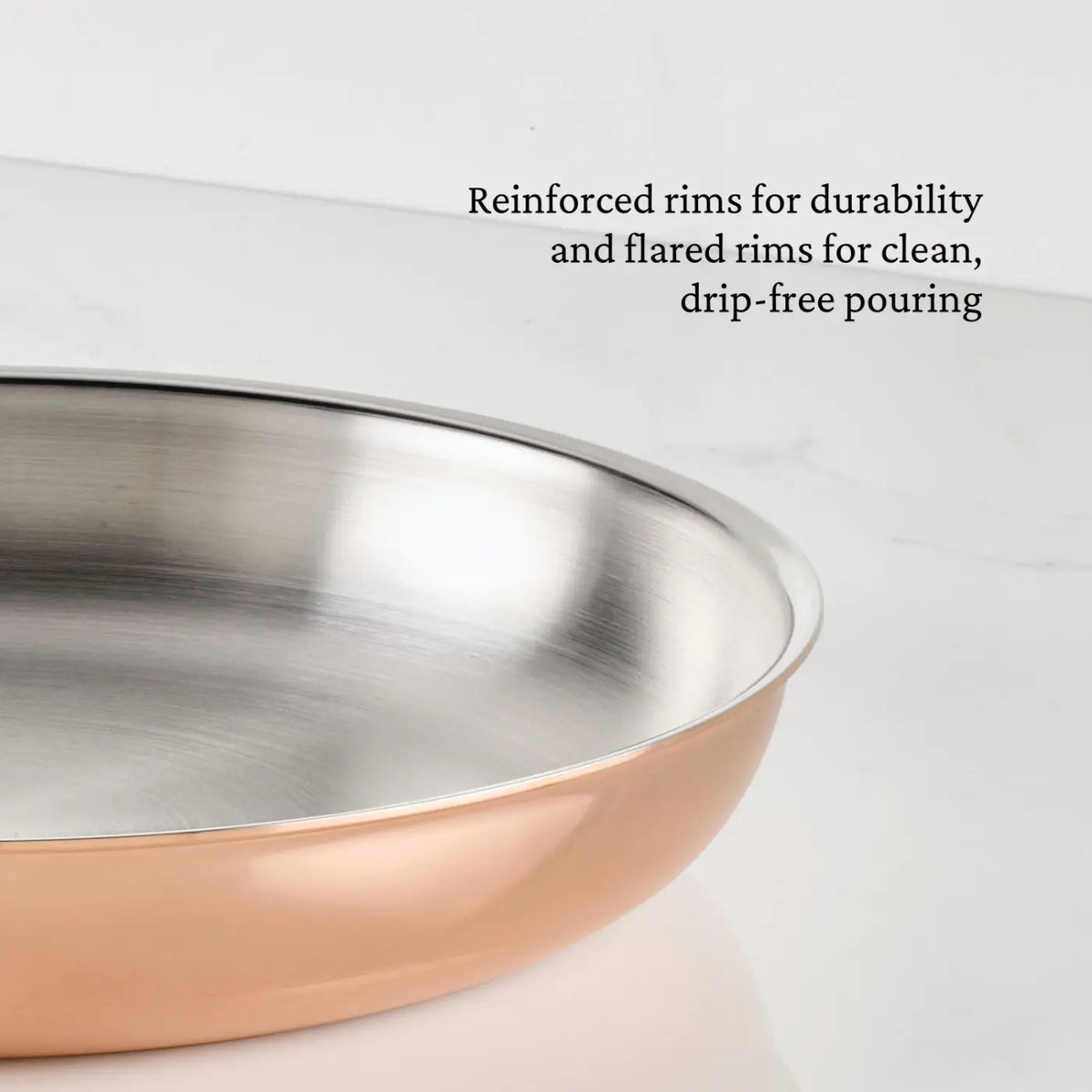 A close-up of a Polished Copper Skillet by CopperBond Aura™, featuring a copper-colored exterior and reinforced, flared rims designed for durability and drip-free pouring. The skillet is set against a white countertop and wall background.