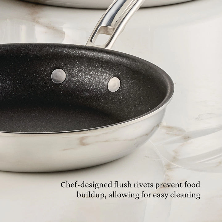 A Polished Clad Stainless Steel 10-Piece Set with TITUM® Nonstick from ProBond Luxe® is shown on a white marble surface. Text below reads, Chef-designed flush rivets prevent food buildup, allowing for easy cleaning.