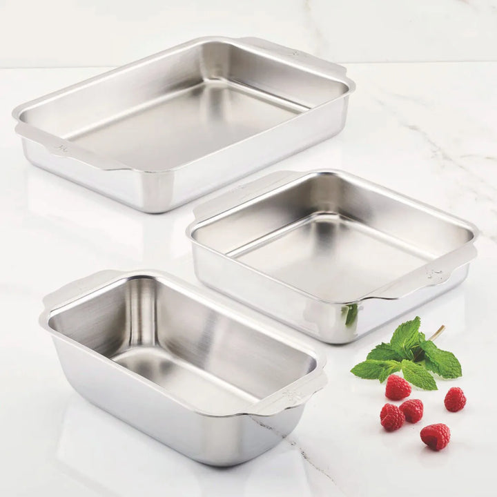 The Hestan OvenBond Tri-Ply 3-Piece Baking Set is displayed on a white marble surface, accented with raspberries and mint leaves next to this stylish, oven-safe bakeware.