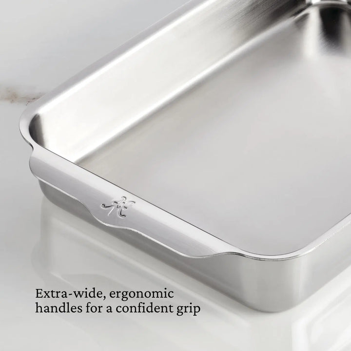 A Hestan OvenBond Tri-ply Rectangular Baker with extra-wide, ergonomic handles and a small engraved logo is shown on a light surface. Caption: Extra-wide, ergonomic handles for a confident grip.