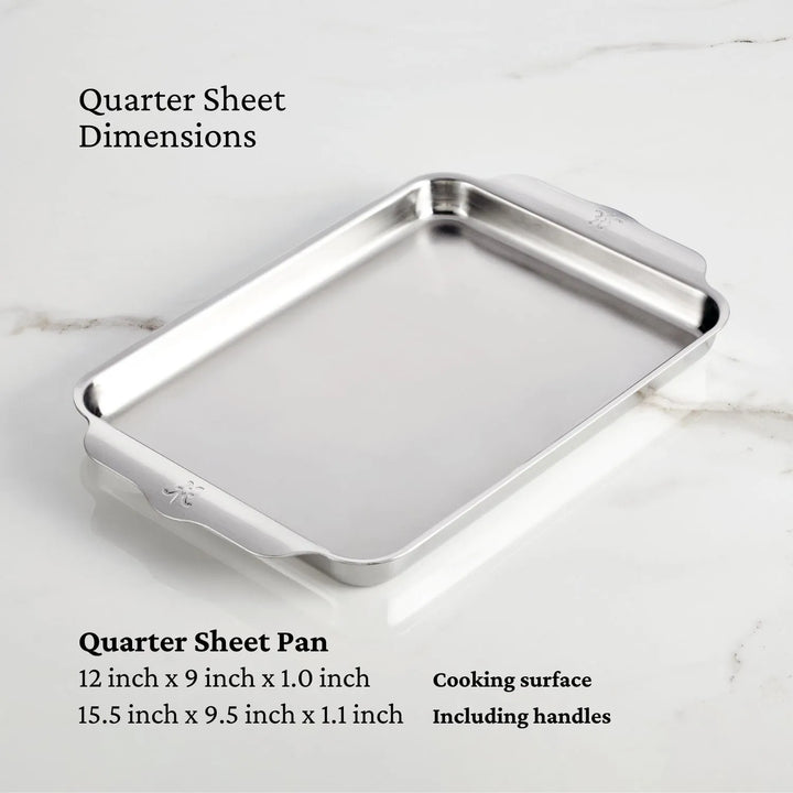 A Hestan OvenBond Tri-ply 3-Piece Set quarter sheet pan rests on white marble. Its cooking surface is 12 x 9 x 1 in, with full dimensions including handles of 15.5 x 9.5 x 1.1 in.
