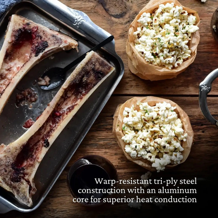 Two roasted bone marrow halves on Hestan OvenBond Tri-Ply Quarter Sheet Pans & Rack, 9"x12", with a spoon and two bowls of herbed popcorn. Warp-resistant tri-ply design ensures superior heat conduction.