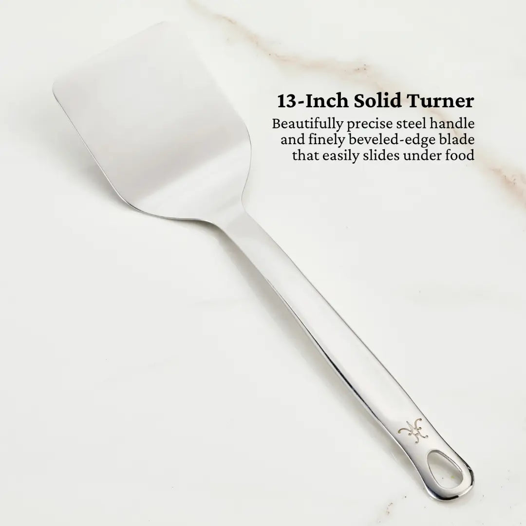 The Deluxe Chefs Tool Set by Hestan Provisions includes a 13-inch stainless steel solid turner spatula with a flat, beveled-edge blade for easy food handling and a handle elegantly adorned with a fleur-de-lis design.