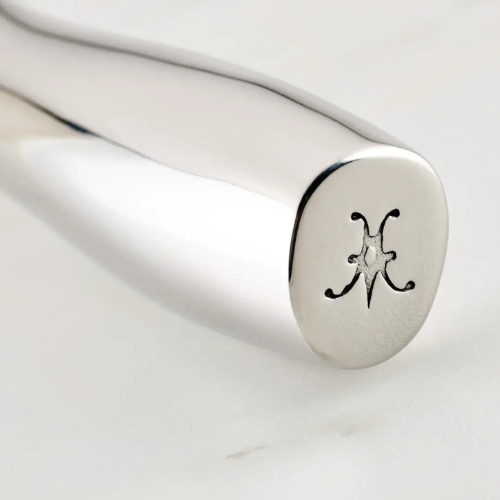 A close-up shows a shiny silver handle made from 18/10 stainless steel with an engraved star-like emblem and curves, symbolizing the Hestan Provisions brand. Favored by Michelin-starred chefs, it belongs to the Ultimate Chefs Tool Set, 8-piece.