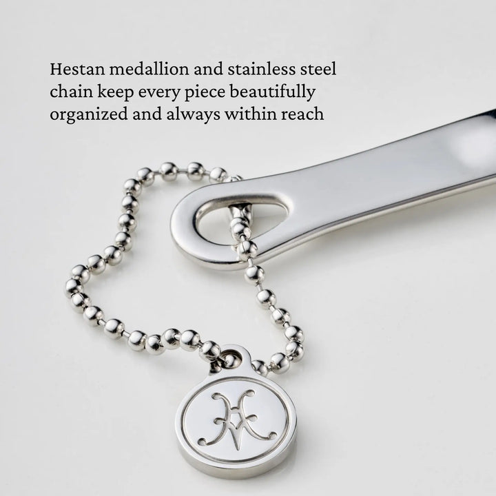 A stainless steel medallion featuring an engraved symbol is secured to a ball chain, which threads through a flat metallic piece. This design reflects the organizational precision of the Hestan Provisions® Odd-Size Measuring Cups Set, 3-Piece, ensuring your tools are always within reach.