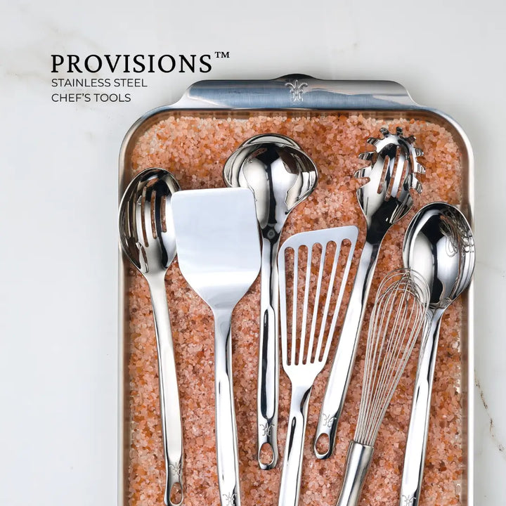 Displayed on a pink salt tray, the Hestan Provisions Chef’s Tools feature premium stainless steel utensils like a ladle, pasta server, spatula, and whisk, with Provisions elegantly placed in the top left corner.