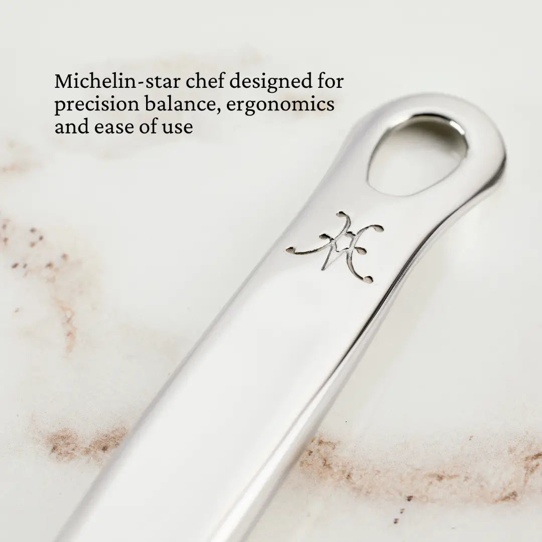 Close-up of the Hestan Provisions 13-inch Pasta Fork, featuring a sleek stainless steel design with an engraved symbol and ergonomic form. Michelin-star chef designed for precision balance and ease of use, set against a signature light, textured background.