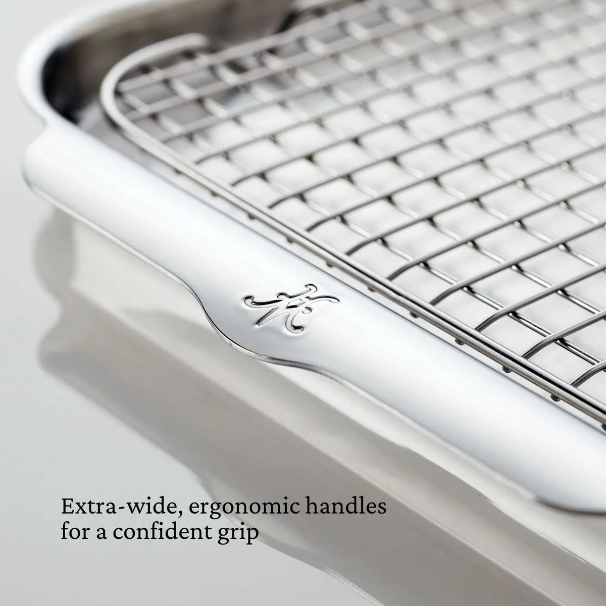 Close-up of a Hestan OvenBond Tri-Ply Medium Sheet Pan & Rack, 12"x15", featuring a perforated rack and extra-wide, ergonomic handles for a confident grip; engraved Hestan OvenBond logo is visible.