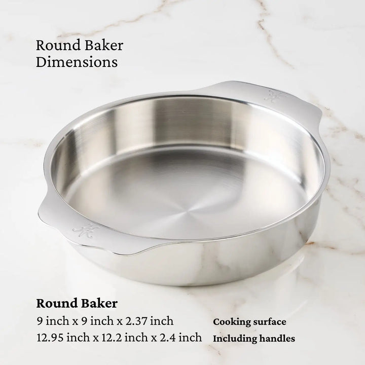 A Hestan OvenBond Round Baker, 9-inch, with handles rests on a white marble surface. Dimensions are 9 x 9 x 2.37 inches (cooking area) and 12.95 x 12.2 x 2.4 inches with handles—a commercial bakeware essential.