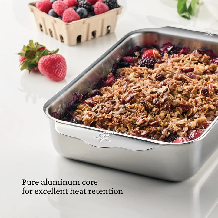 The Hestan OvenBond Tri-ply Small Rectangular Baker, filled with berry crumble, sits on a white counter with strawberries around. Text on the image reads: Oven safe to 600°F for excellent heat retention.