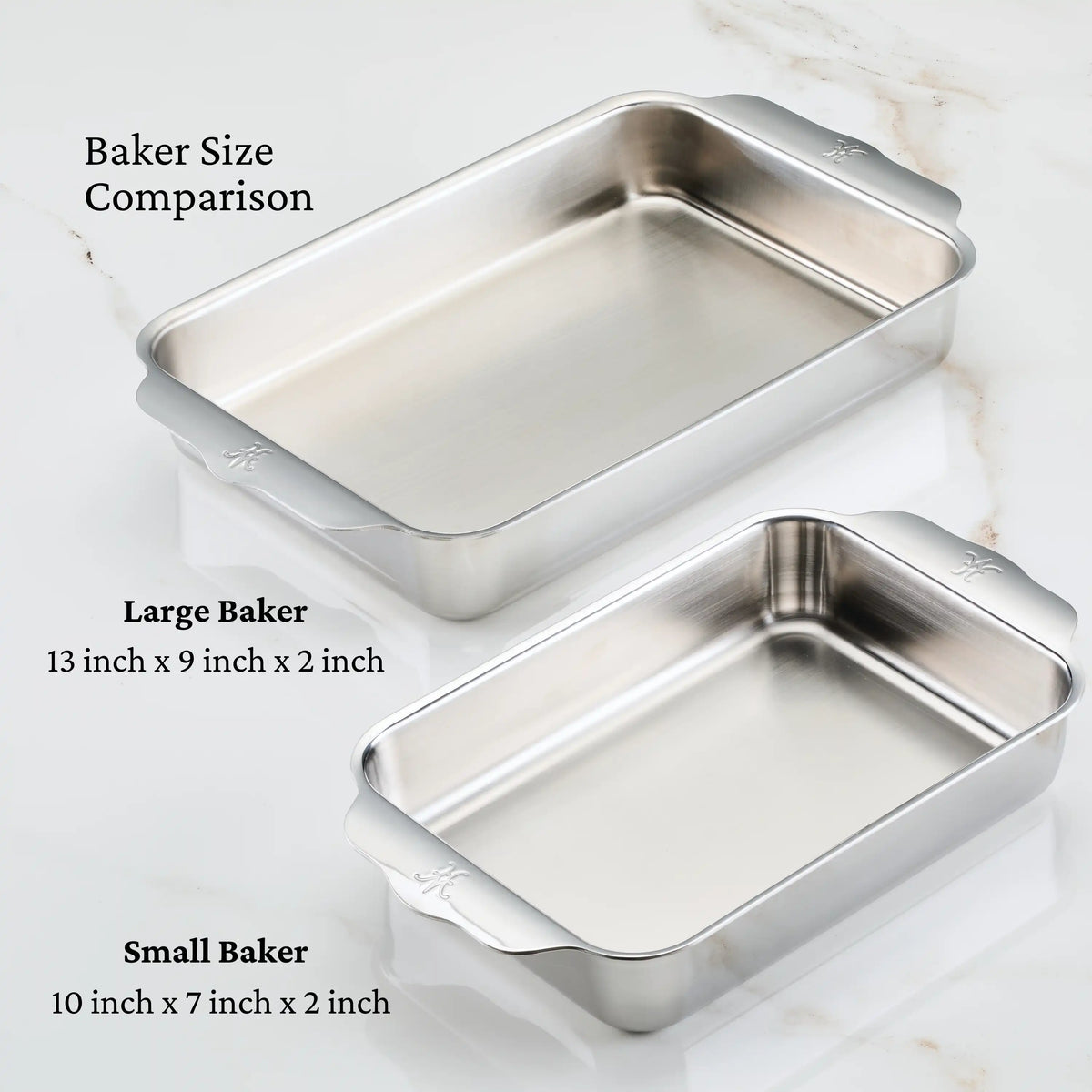 Two Hestan OvenBond Tri-ply Small Rectangular Bakers, measuring 13" x 9" x 2" and 10" x 7" x 2", with handles, are displayed on white marble. Both clad stainless steel bakers are oven safe up to 600°F.