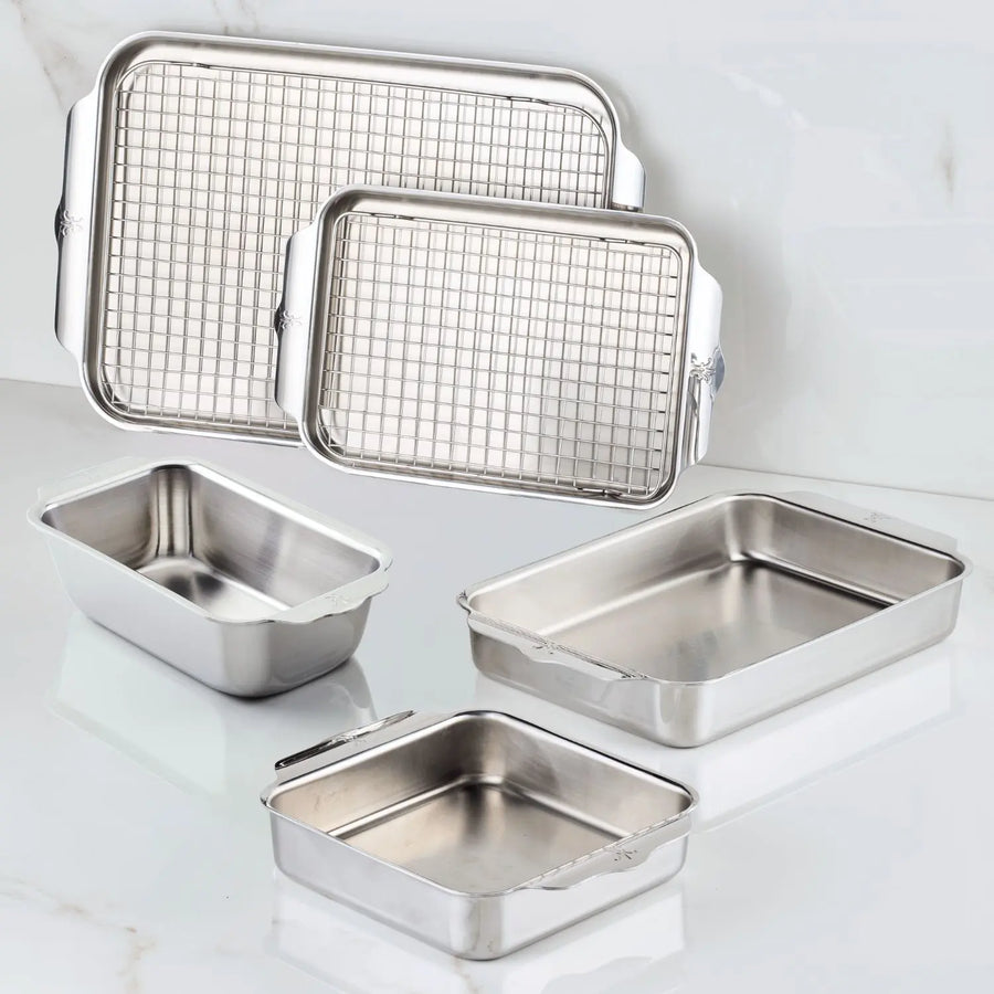 The Hestan OvenBond Tri-ply Gourmet Essentials Stainless Steel 7-piece Set is shown on a white surface, with two pans featuring metal cooling racks and others empty, highlighting this durable and versatile bakeware collection.