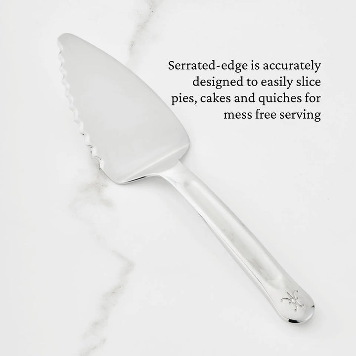 A Hestan Provisions® 10.5-inch Stainless Steel Pie & Cake Server with a serrated edge is displayed on a white marble surface. Text reads: The precisely crafted serrated edge easily slices pies, cakes, and quiches for mess-free serving—a perfect addition to your Provisions Serving Tools collection.
