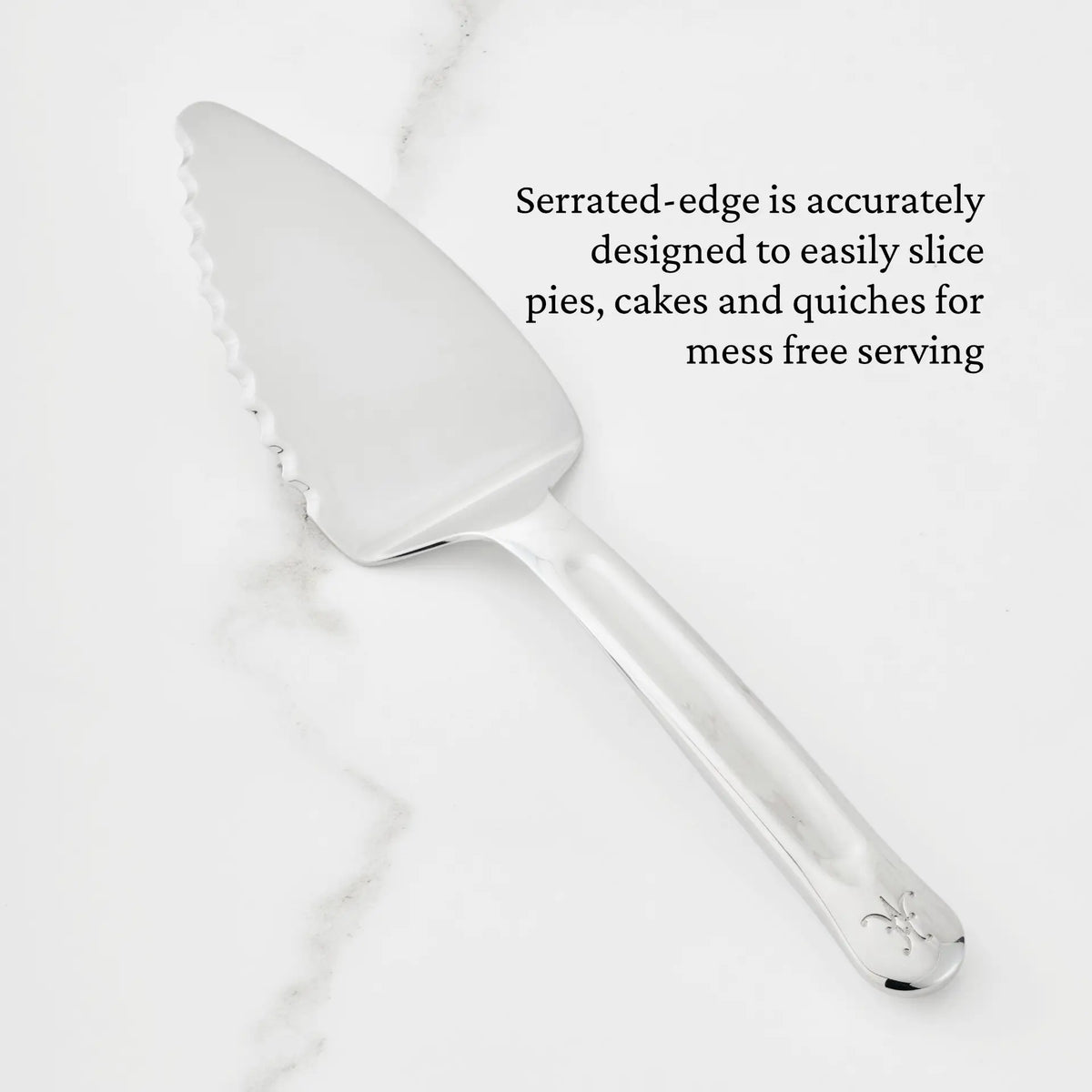A Hestan Provisions® 10.5-inch Stainless Steel Pie & Cake Server with a serrated edge is displayed on a white marble surface. Text reads: The precisely crafted serrated edge easily slices pies, cakes, and quiches for mess-free serving—a perfect addition to your Provisions Serving Tools collection.